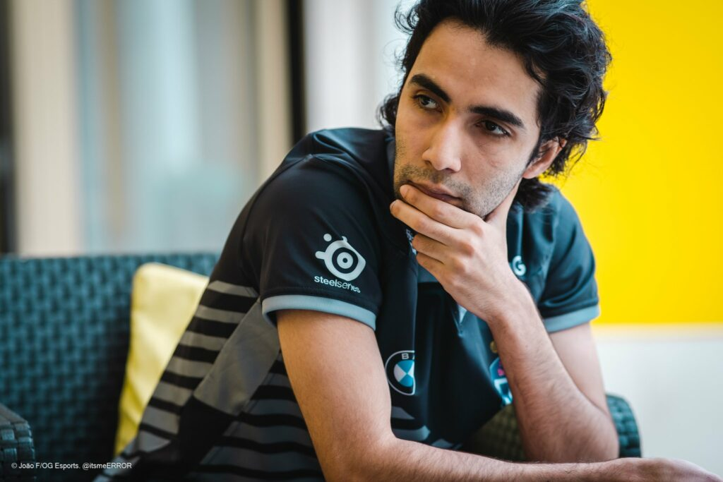 Esports player, Sumail, in a team jersey sitting thoughtfully with hand on chin.