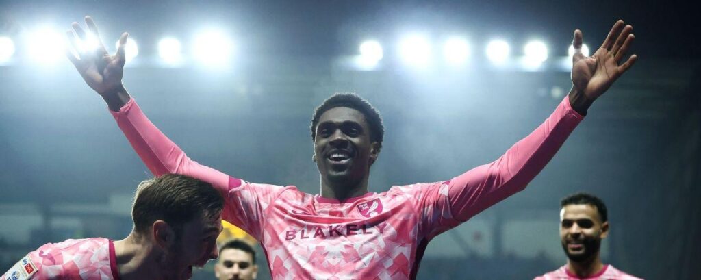 Mohamed Toure celebrating with raised arms after a football victory under stadium lights
