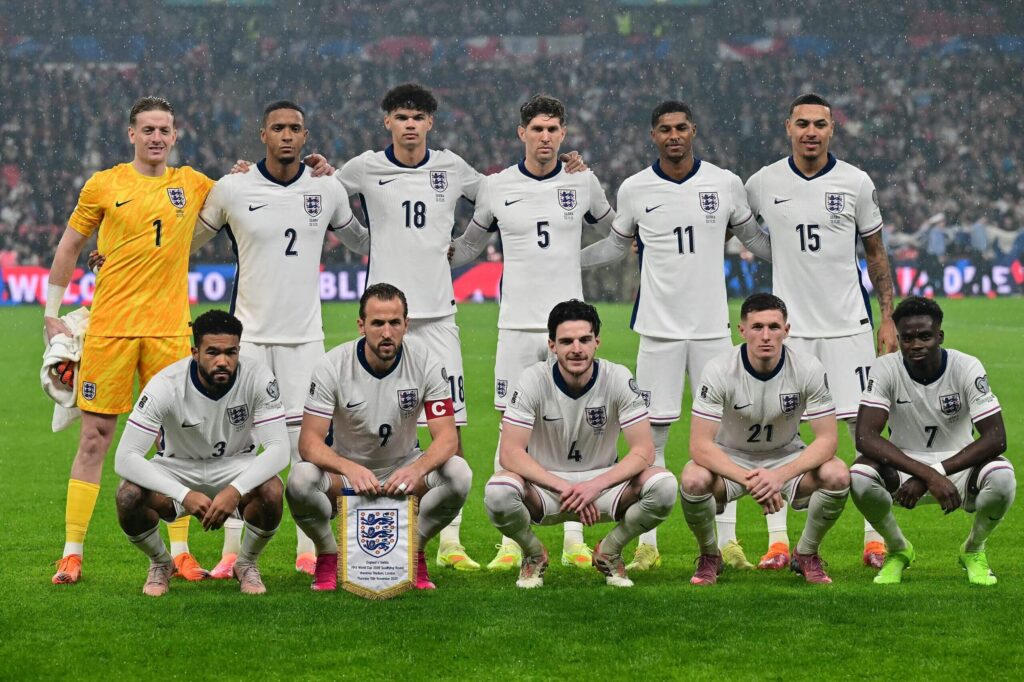 England national football team players in white kits posing together on the pitch before a match in rainy conditions.