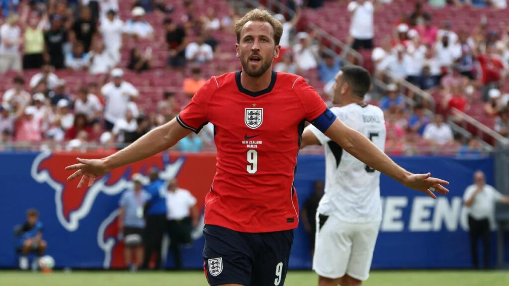 England national team forward, Harry Kane, in a red number 9 kit celebrating with arms outstretched during a football match.