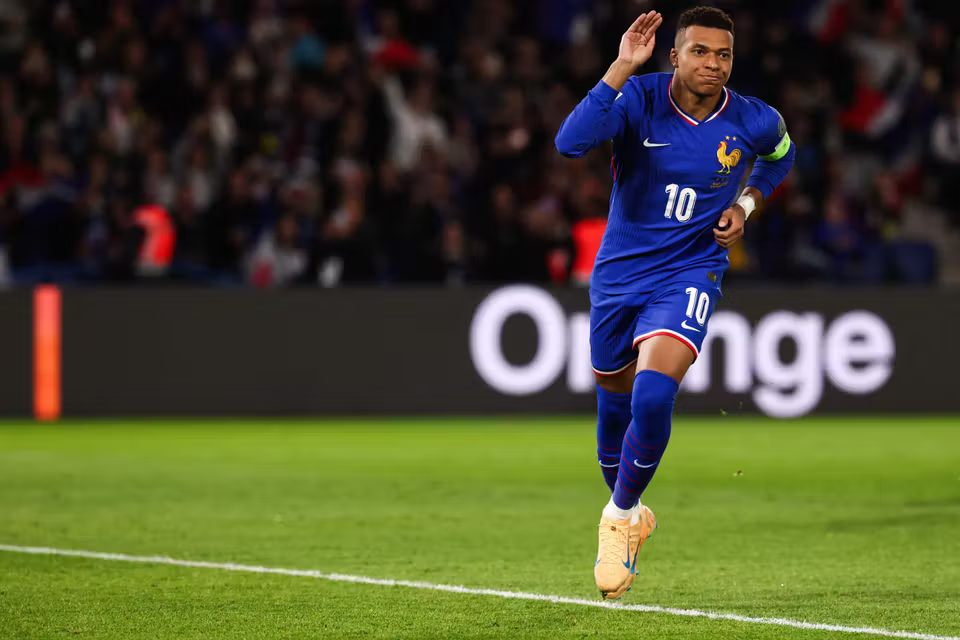 France national team forward, Kylian Mbappe, in a blue number 10 kit celebrating on the pitch during a football match.