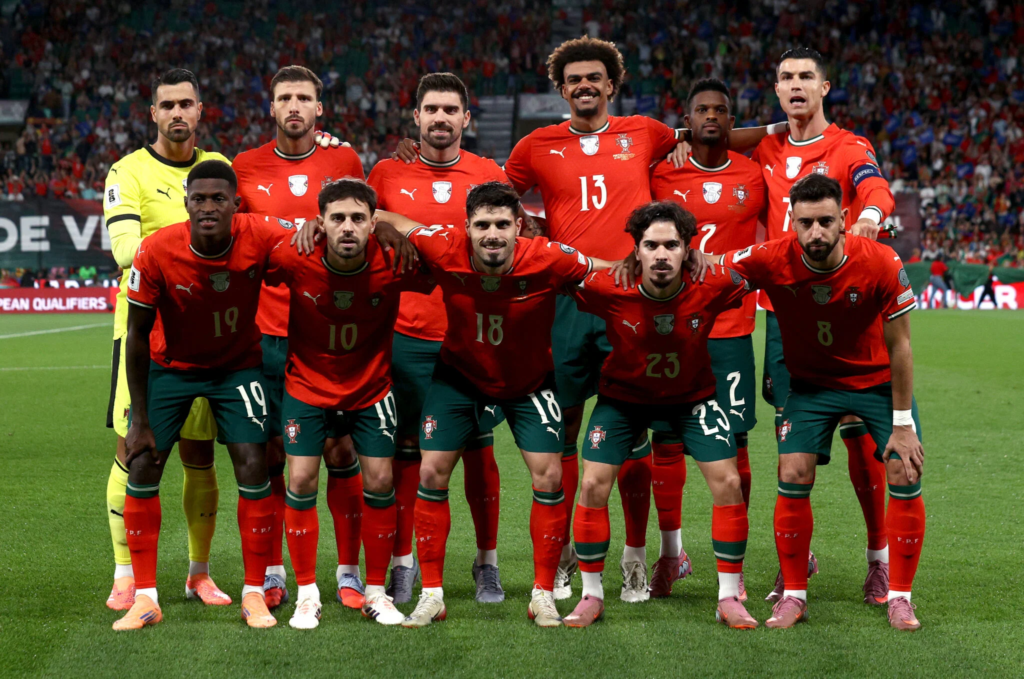 Portugal national football team players in red and green kits posing together on the pitch before a match.