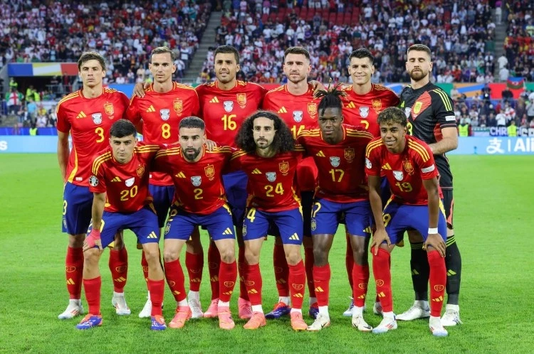 Spain national football team players in red and blue kits posing together on the pitch before a match.